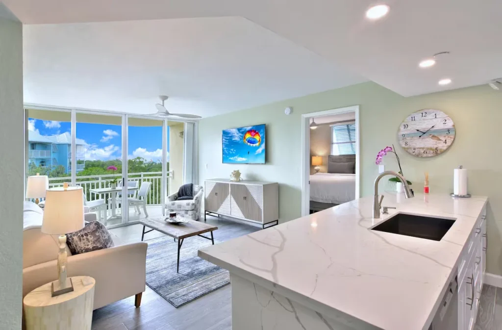 Modern condo interior with a white quartz kitchen island, a living room, and large balcony doors