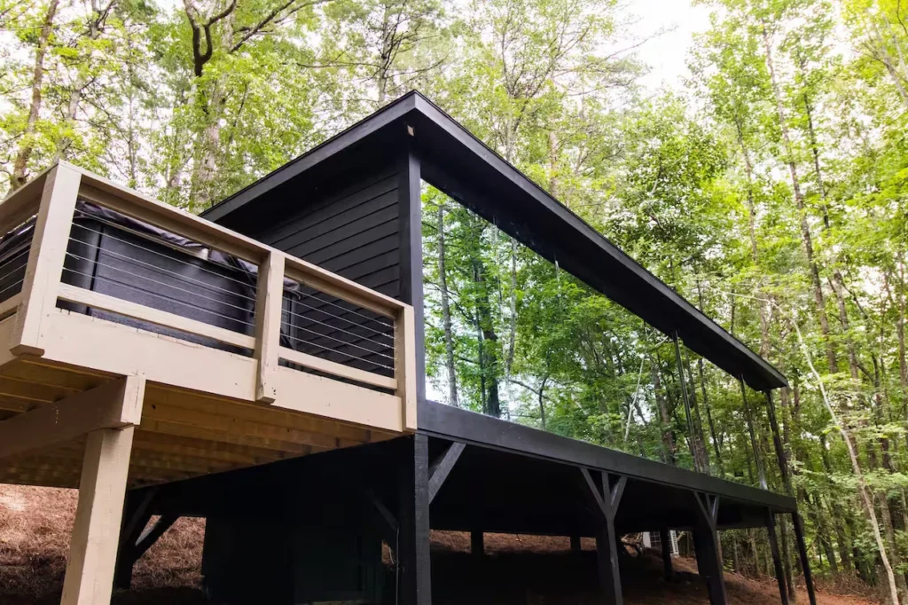 Modern black cabin with a massive glass wall and an elevated wooden deck surrounded by trees