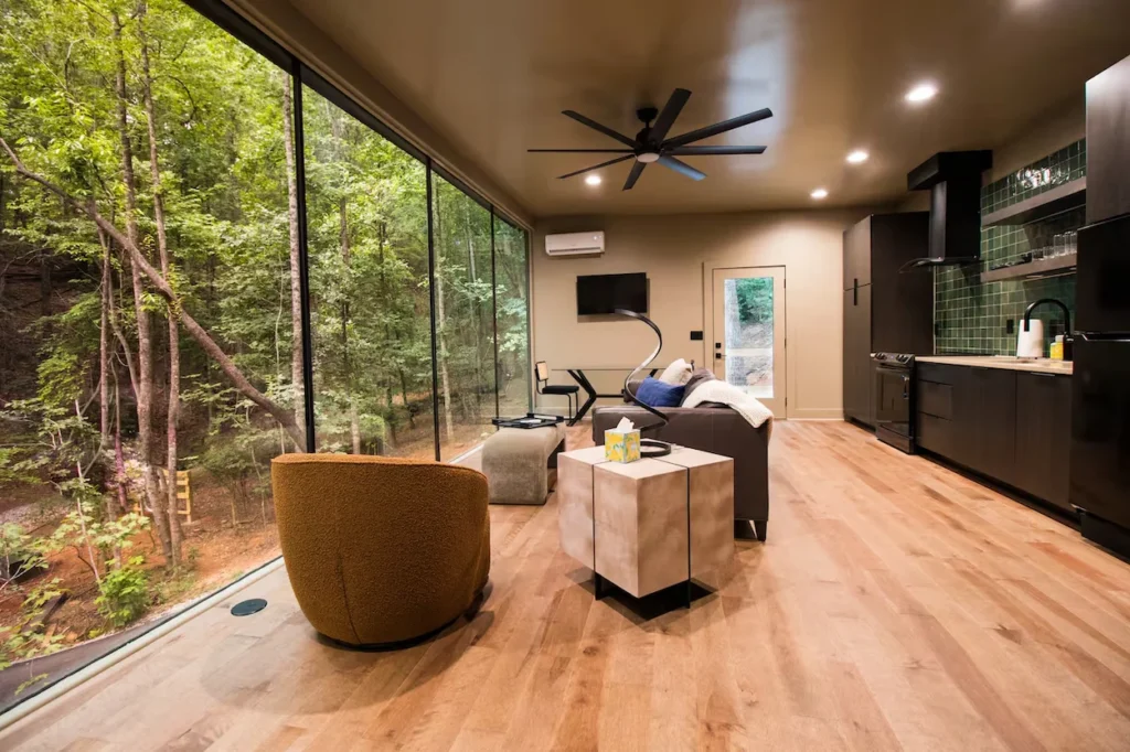 Modern cabin interior with a floor-to-ceiling glass wall showcasing a dense green forest