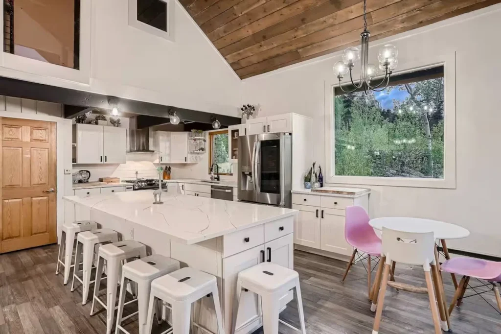 White marble island with stools in a modern cabin kitchen featuring a vaulted wood ceiling