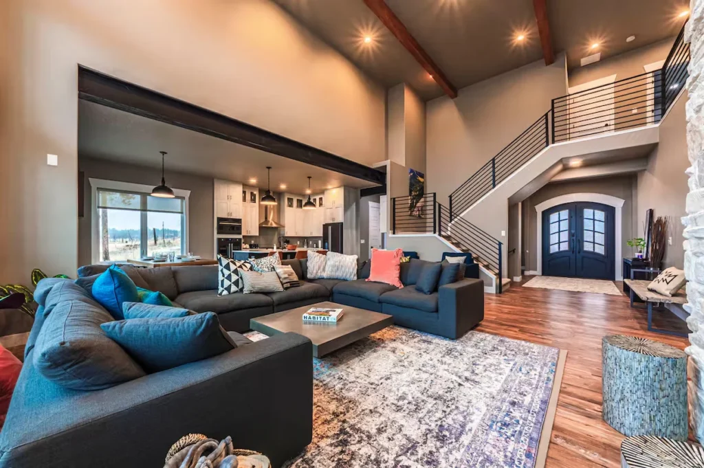 Large grey sectional sofa on a patterned rug in a modern living room with a prominent staircase