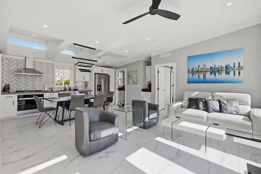 Modern open-concept white living room and kitchen with grey armchairs and a glass coffee table