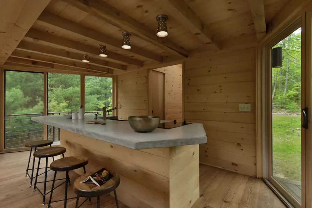 Modern cabin kitchen with a concrete island bar, wood stools, and wood walls