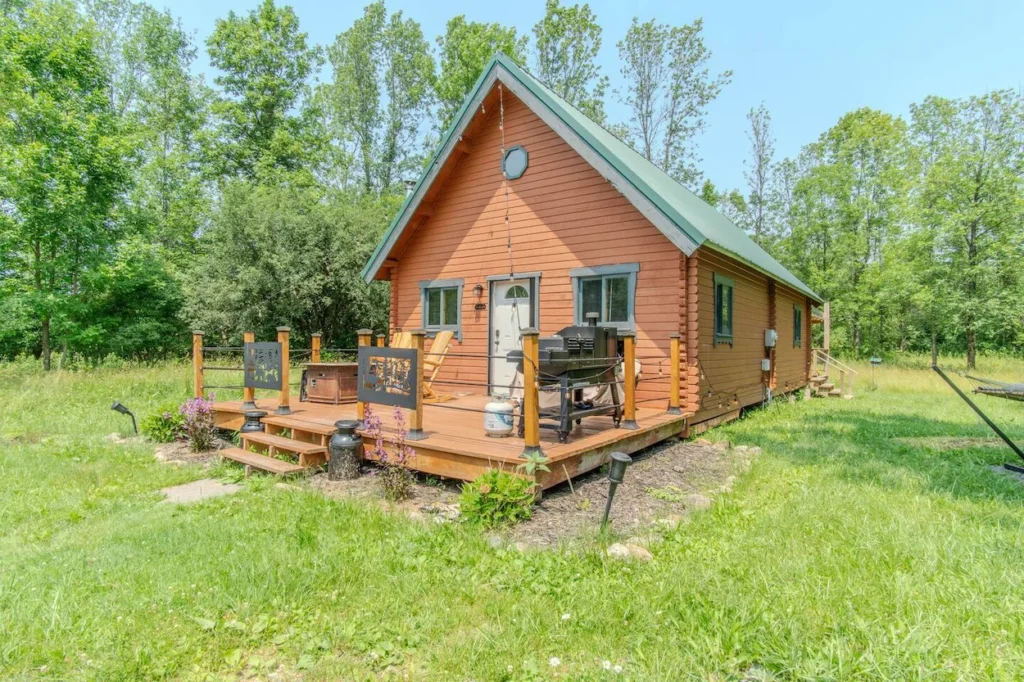 Small wooden log cabin with a front porch deck sitting in a grassy field