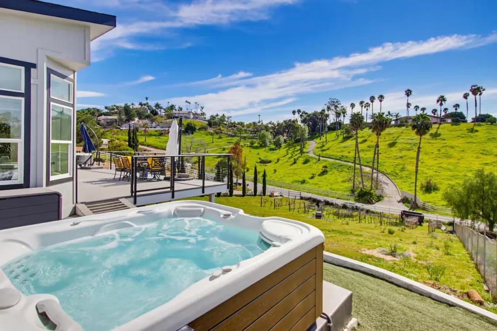 Bubbling outdoor hot tub on a deck overlooking rolling green hills with palm trees