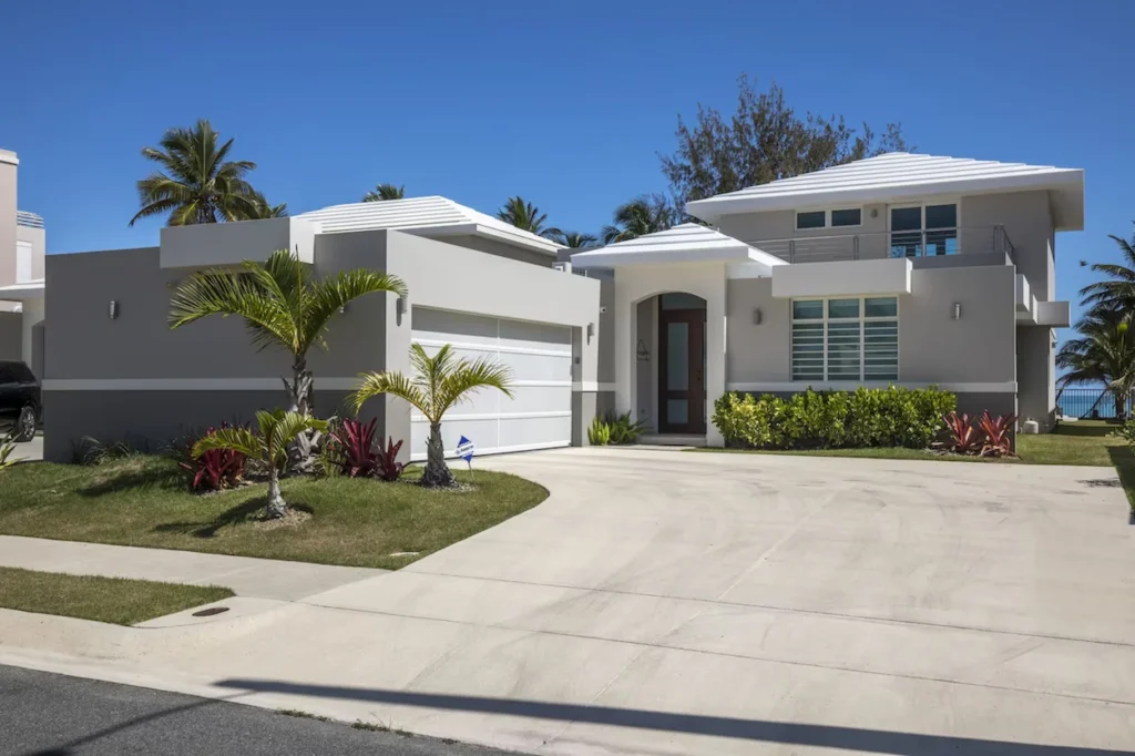 Modern two story gray coastal vacation home with a paved driveway and palm trees under a clear blue sky