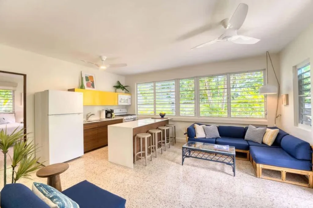 An open-concept living space with a blue sectional sofa, a kitchen island with stools, and yellow cabinetry