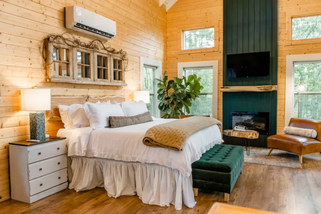 Cozy cabin bedroom with a king bed, wood-paneled walls, and a dark green fireplace