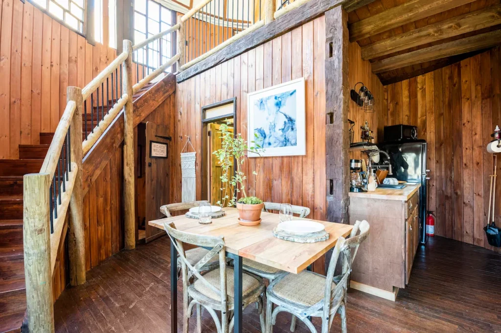 Rustic wood paneled dining and kitchen area with a wooden table, log staircase, and small kitchenette