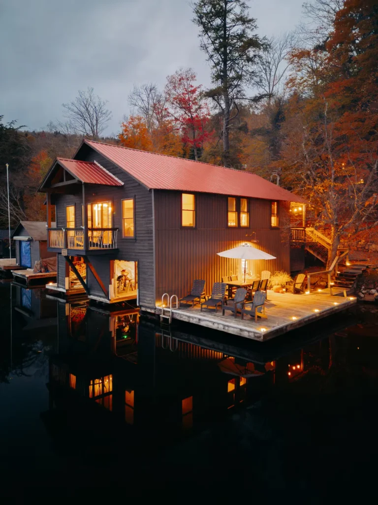 Two-story boathouse cabin with a red metal roof and illuminated floating dock