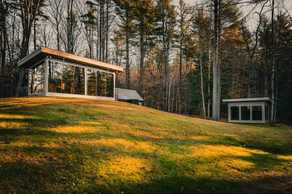 Vermont Mirror House featuring modern glass pavilions on a grassy slope surrounded by tall pine trees