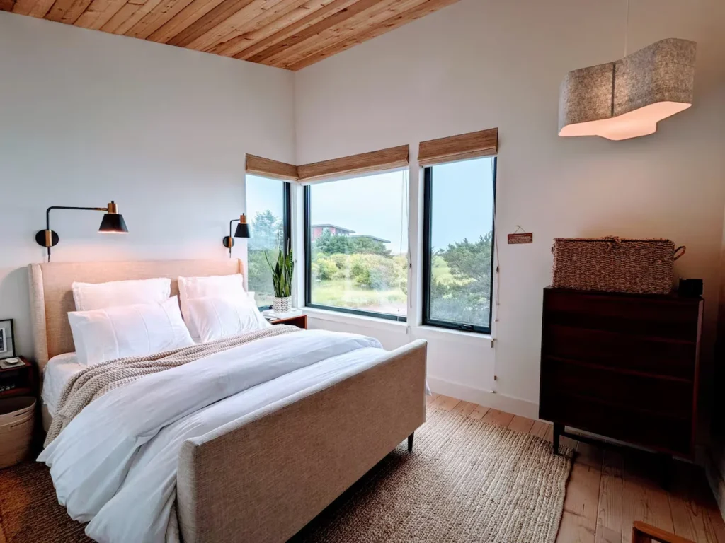 Modern coastal bedroom with a fabric bed frame, wooden ceiling, and large windows