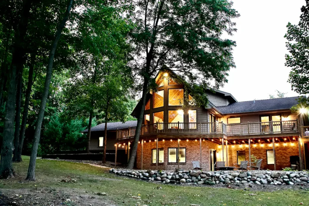 A large timber and brick lodge with glowing windows and a tiered deck at twilight
