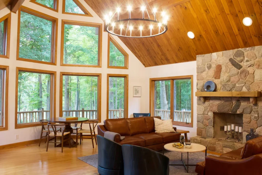 A rustic cabin living room with a large stone fireplace, leather sofas, and a wall of windows