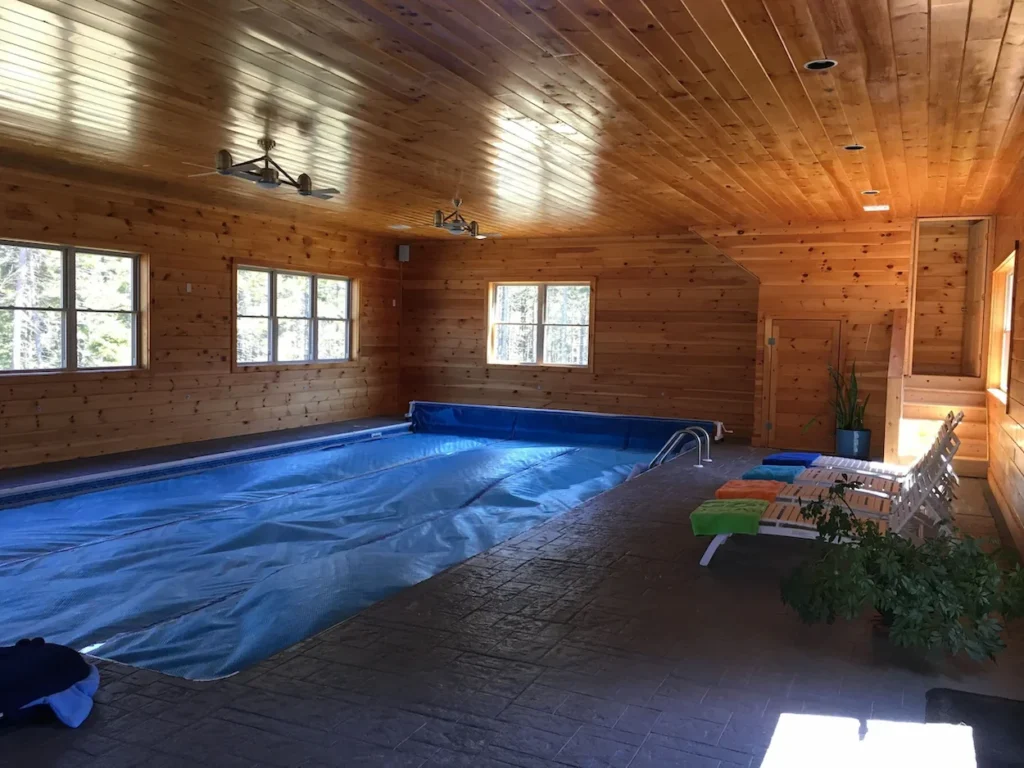 Large indoor lap pool with a blue safety cover in a wood-paneled cabin room