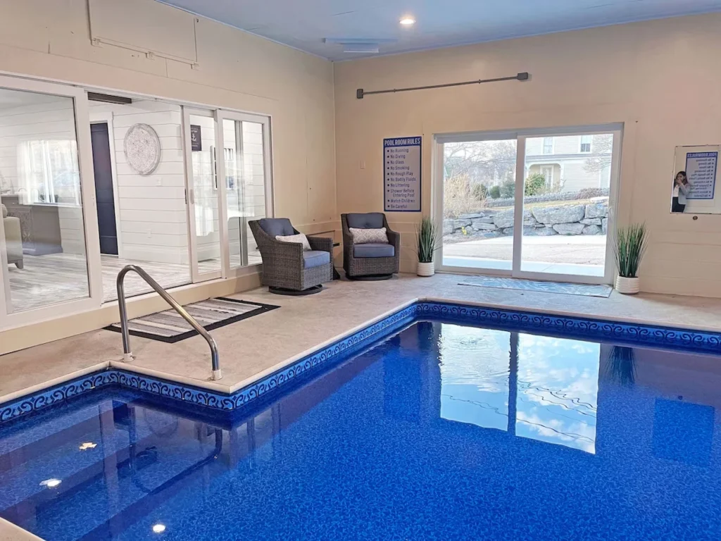Private indoor swimming pool room with blue tile, lounge chairs, and sliding glass doors leading outside