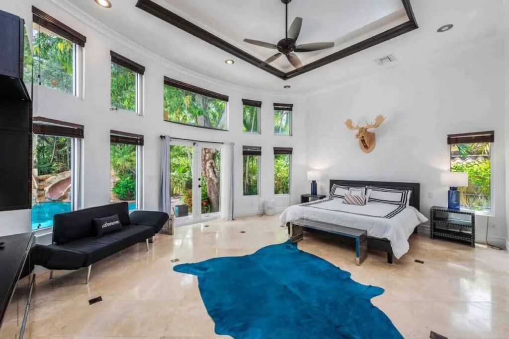 Spacious luxury master bedroom with a bright pool view, large bed, and a vibrant teal hide rug