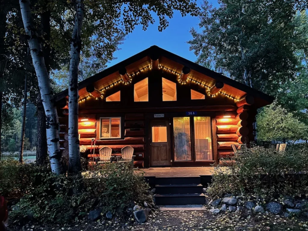 A wooden log cabin house exterior at twilight decorated with warm roofline string lights