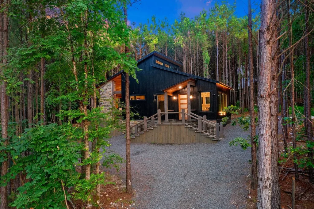 Modern black vertical siding cabin with stone accents and wooden stairs nestled in a dense pine forest