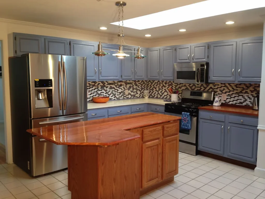 Kitchen with light purple-gray cabinets, stainless steel appliances, a tile backsplash, and a polished wood island