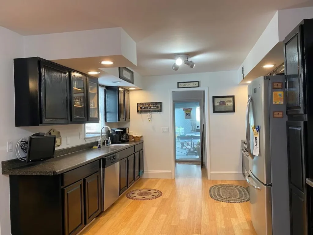 Kitchen with black wood cabinets, stainless steel appliances, dark countertops, and light hardwood floors