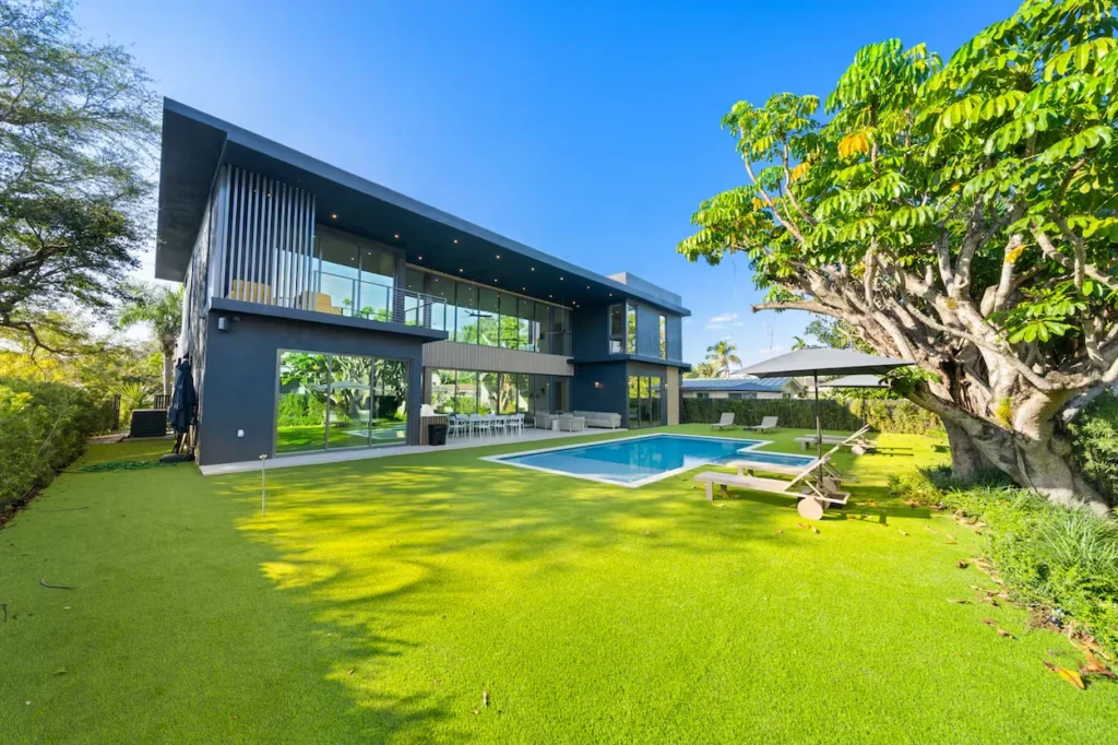 Modern dark grey two-story mansion with a rectangular swimming pool and large green lawn