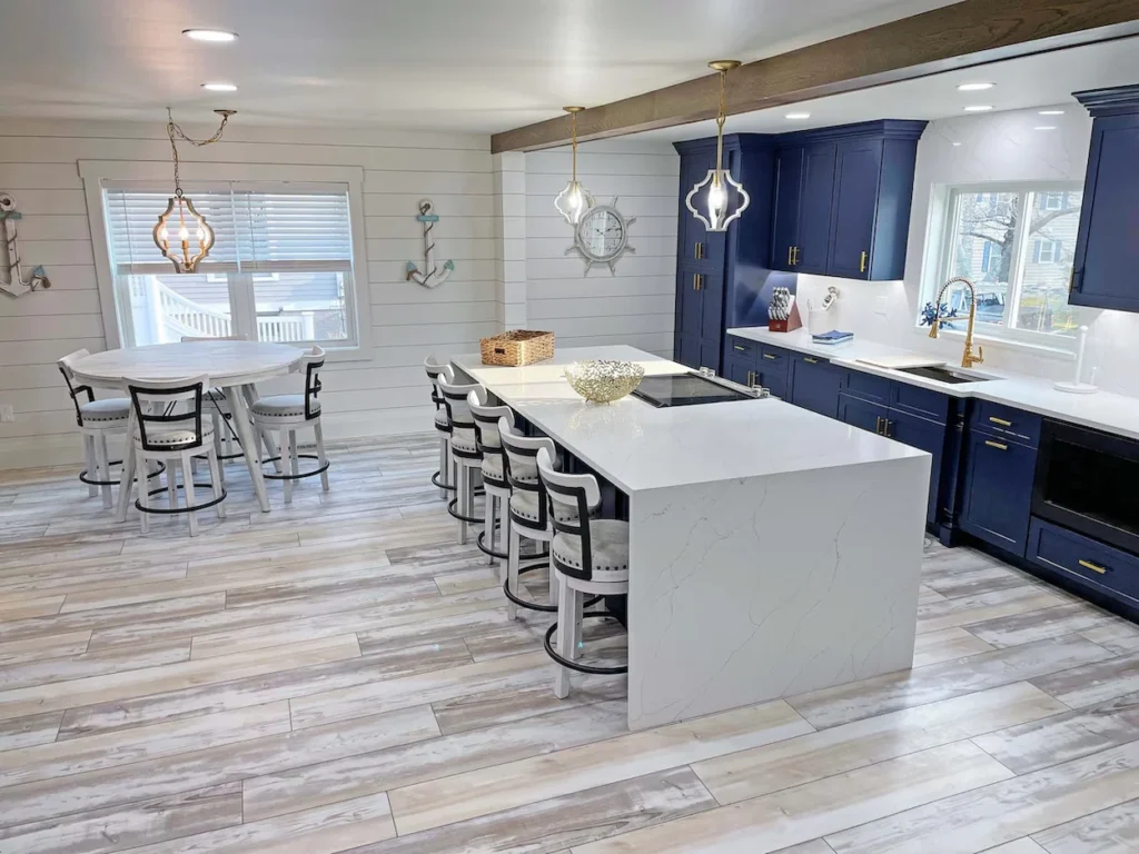 Modern coastal kitchen featuring navy blue cabinets, a white quartz waterfall island with barstools, and light wood flooring