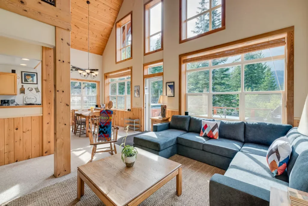 Open cabin living room with a large blue sectional couch, vaulted wood ceilings, and high windows