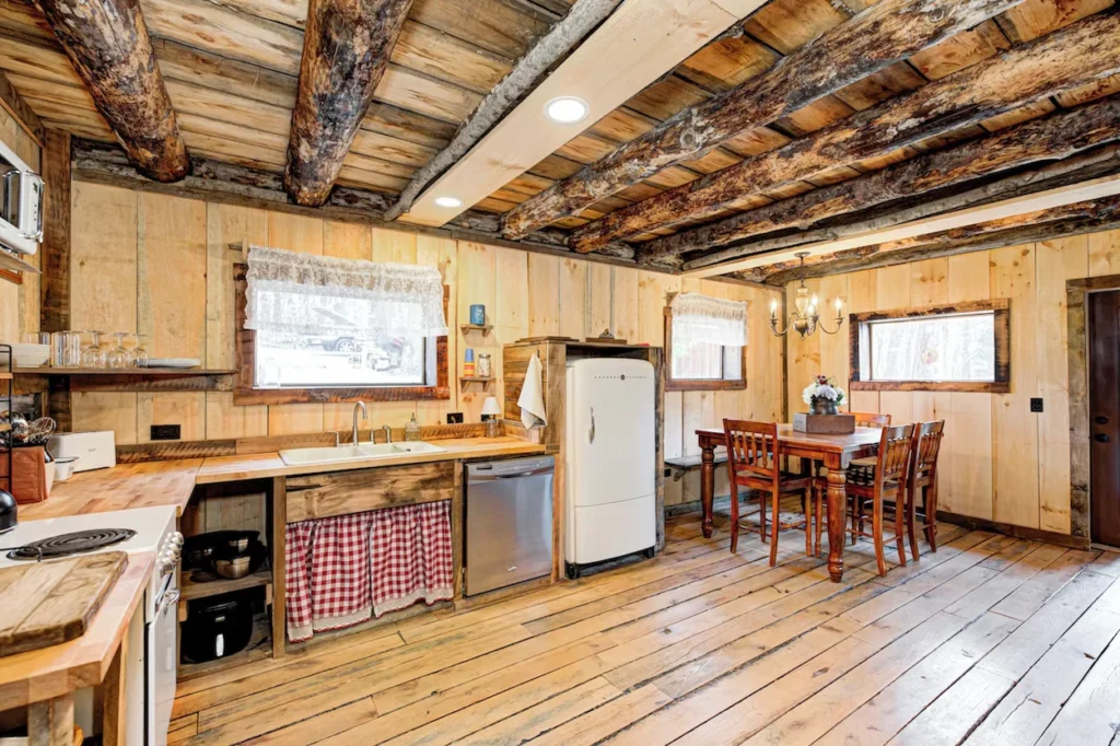A rustic cabin kitchen with wooden counters, a vintage white refrigerator, and a wooden dining table set