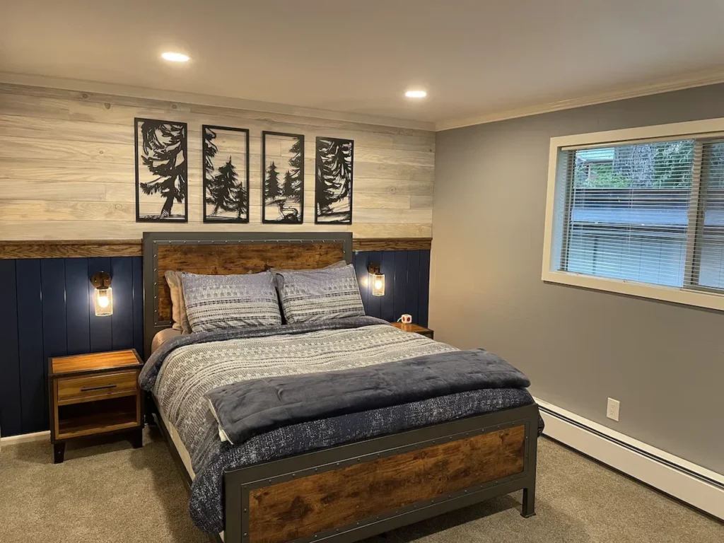 A bedroom with a rustic wood and metal bed frame, blue wainscoting, and four black framed tree silhouette art pieces