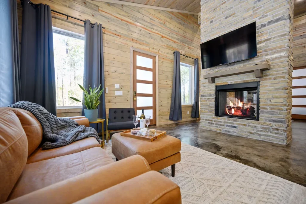 Cabin living room featuring a tan leather sofa, an ottoman with a wine tray, and a large stone fireplace