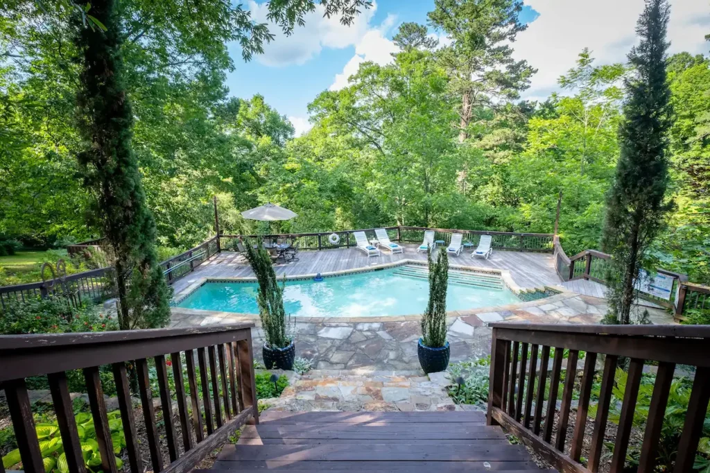 Backyard swimming pool surrounded by a wooden deck and dense green trees