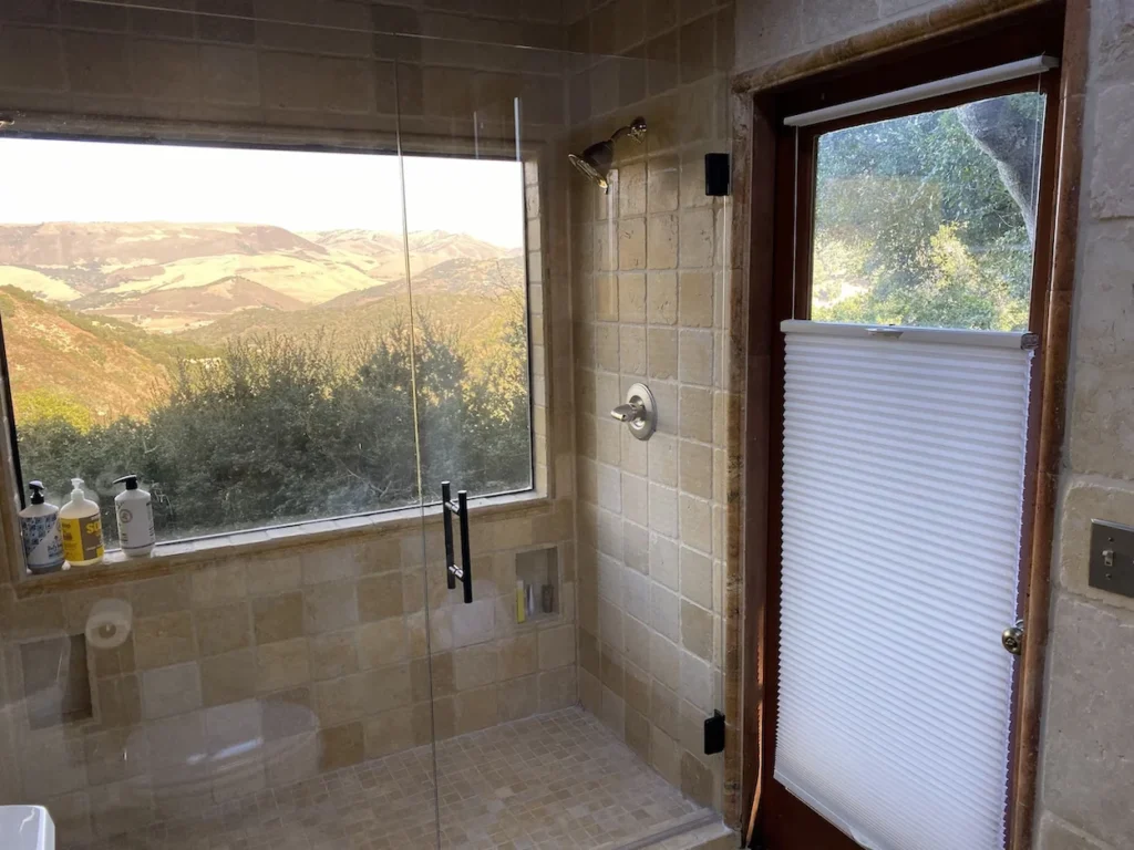 Stone tile walk-in shower with a large window looking out onto a mountain valley landscape