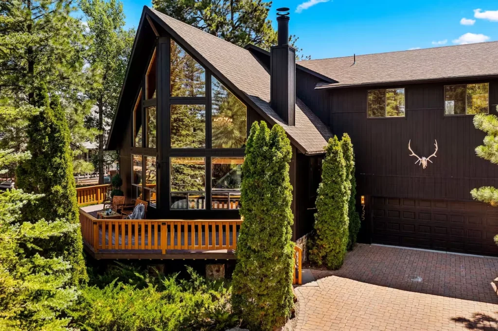Exterior of a dark brown modern A-frame cabin with a wooden deck and brick driveway