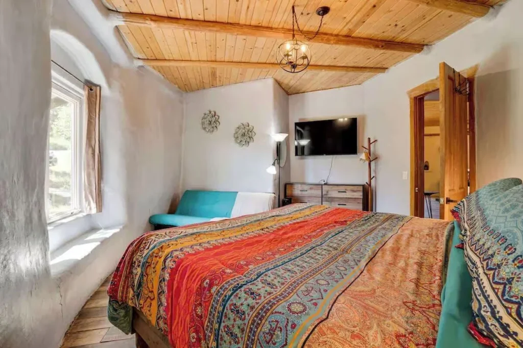Cozy bedroom with textured earth walls, a wood plank ceiling, and a colorful patterned bedspread