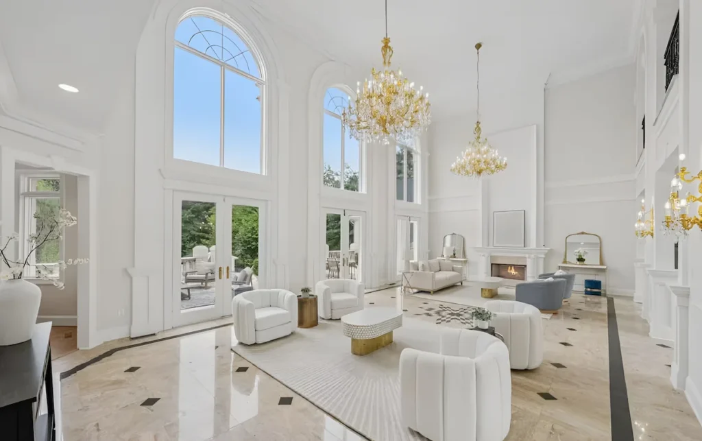 Grand mansion living room with white tub chairs, marble flooring, and crystal chandeliers under high ceilings