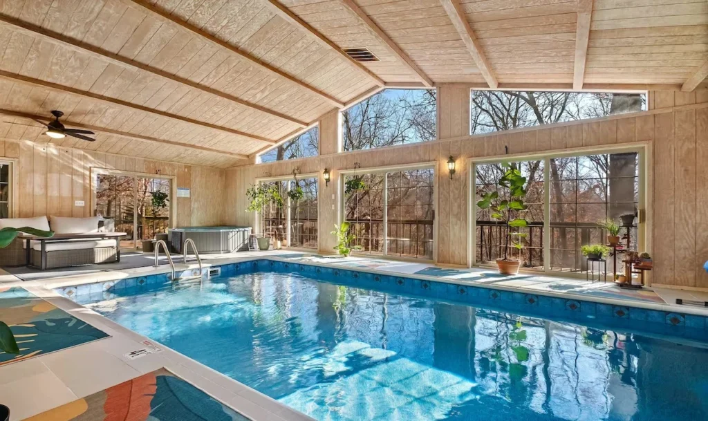 Indoor swimming pool in a wood-paneled room with large windows and a hot tub