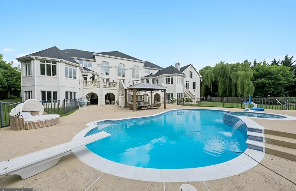 Large backyard of a white multi-story mansion featuring a swimming pool, diving board, and gazebo