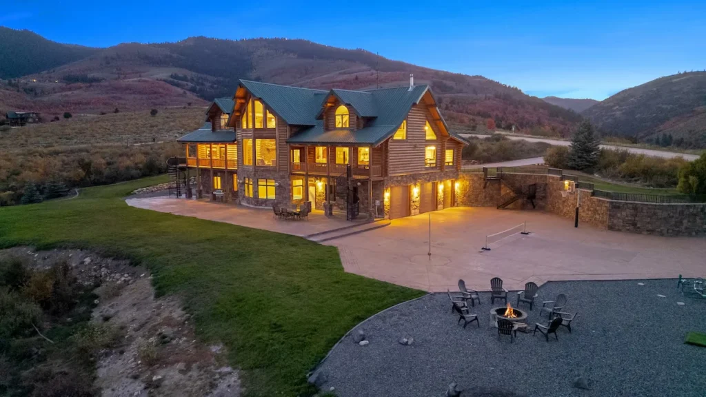Aerial view of a luxury log home at dusk featuring a sports court and a lit fire pit