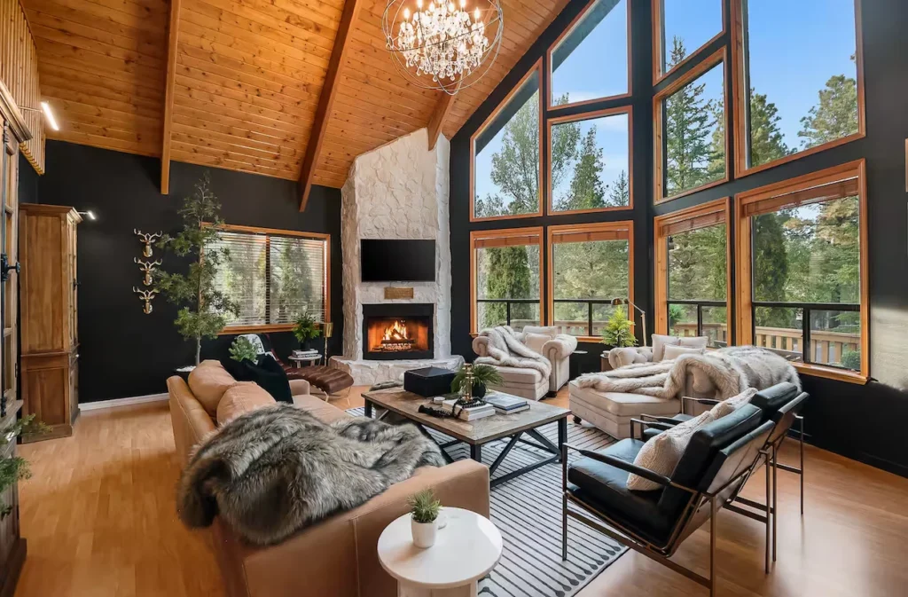 Modern cabin living room with black walls, a white stone fireplace, and floor-to-ceiling windows