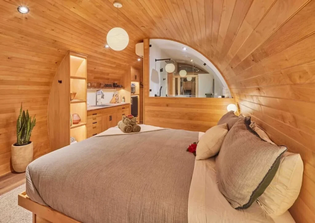 A modern curved wood paneled bedroom inside a treehouse with a large bed and a small kitchenette