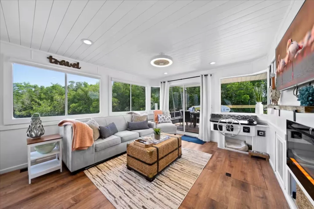 Bright houseboat living room with a gray couch and a corner steering wheel helm