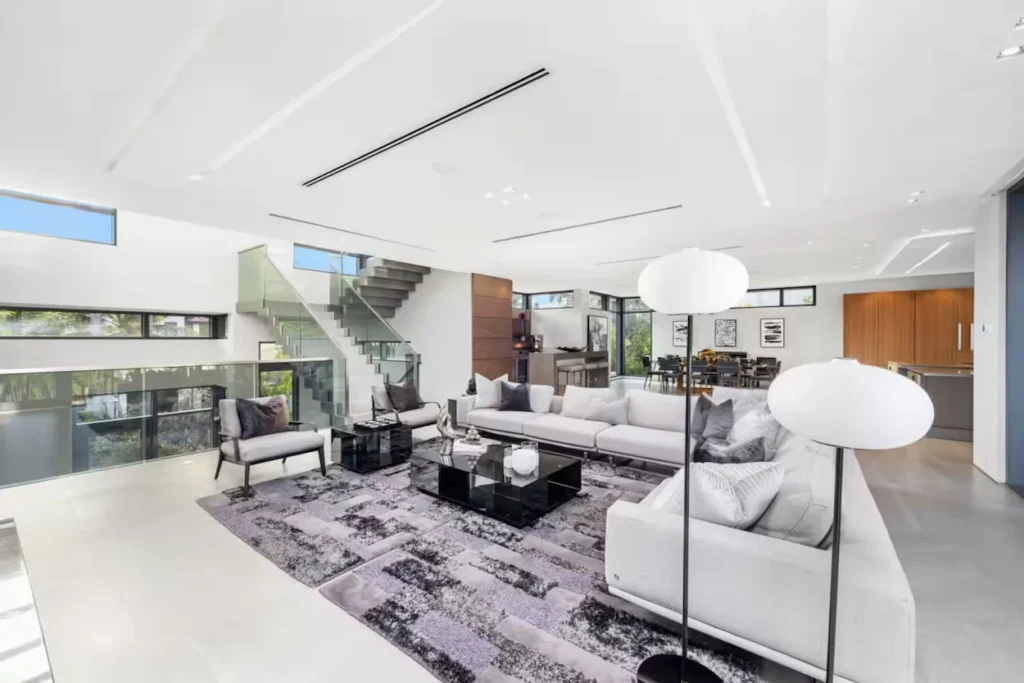Bright modern living room with a white sectional sofa, glass-panel staircase, and black coffee table