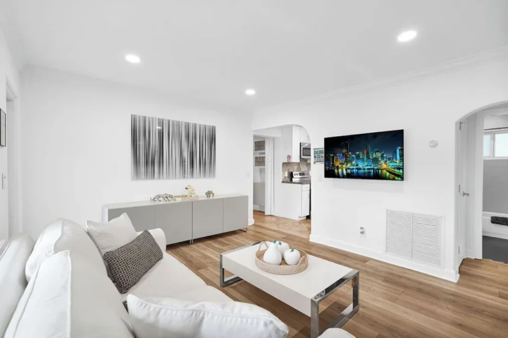 White living room with a white couch, wooden floors, and a wall-mounted TV