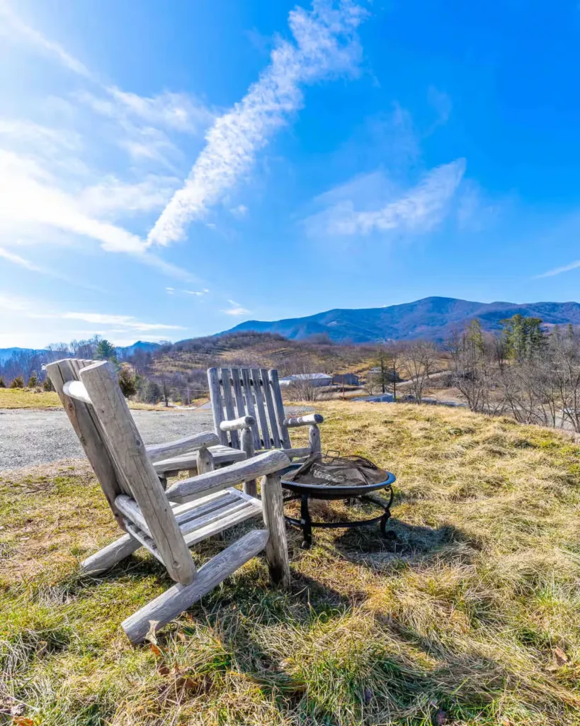Two wooden Adirondack chairs next to a metal fire pit overlooking scenic mountains