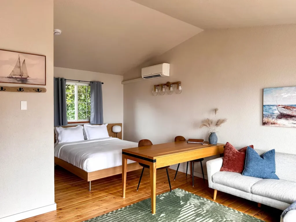 Studio with queen bed, dining table, and small grey sofa on wood floors