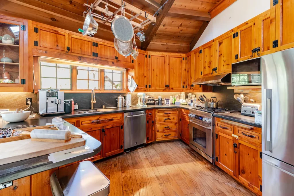 Rustic kitchen with wood cabinets, dark countertops, stainless steel appliances, and a hanging pot rack