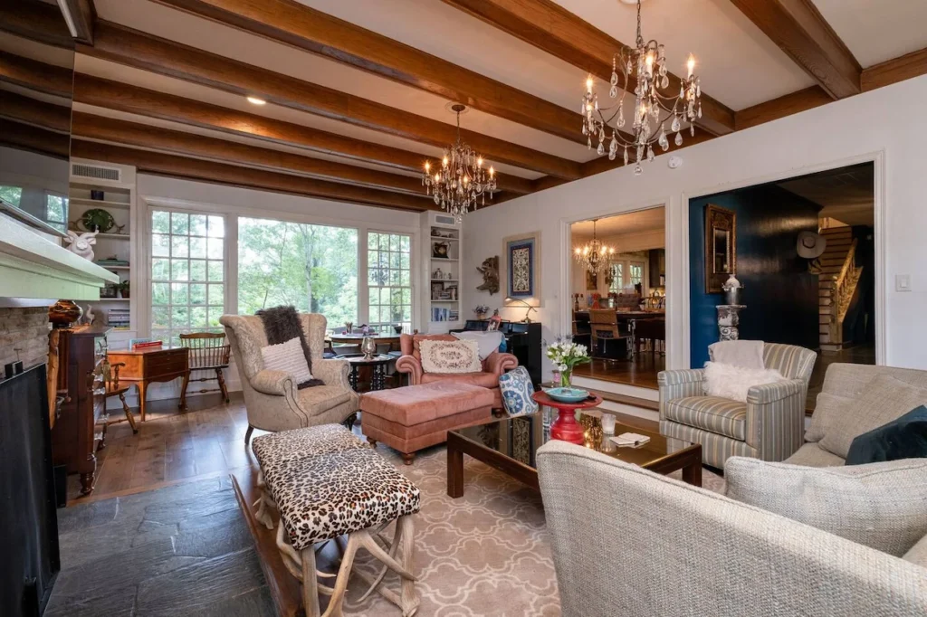 Living room with exposed wood ceiling beams, crystal chandeliers, armchair seating, and large windows