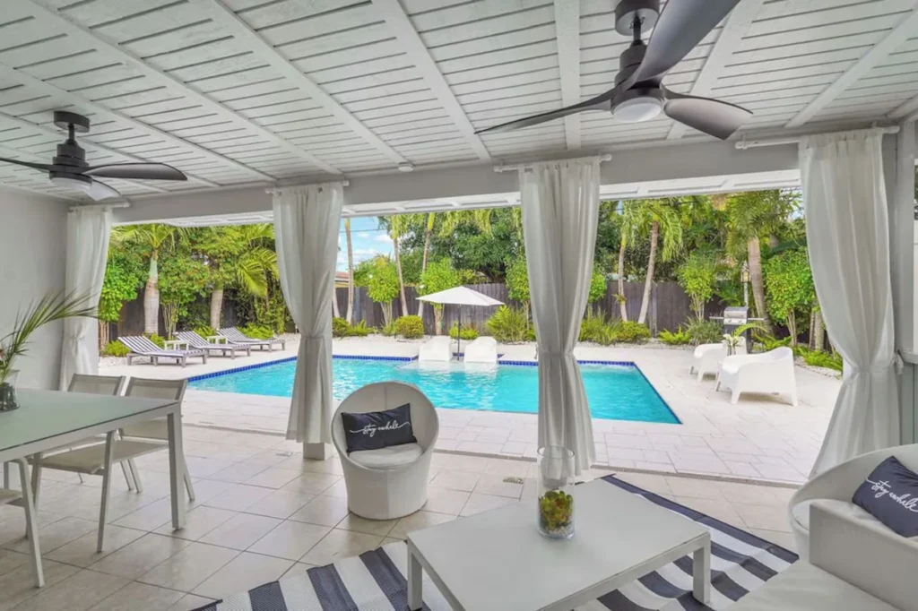 Covered patio with white curtains and ceiling fans overlooking a backyard swimming pool