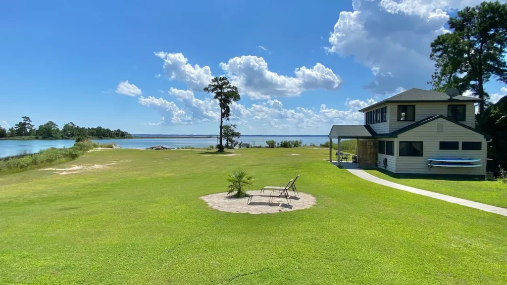 Waterfront cottage with a large green lawn leading to a river bay under a blue sky
